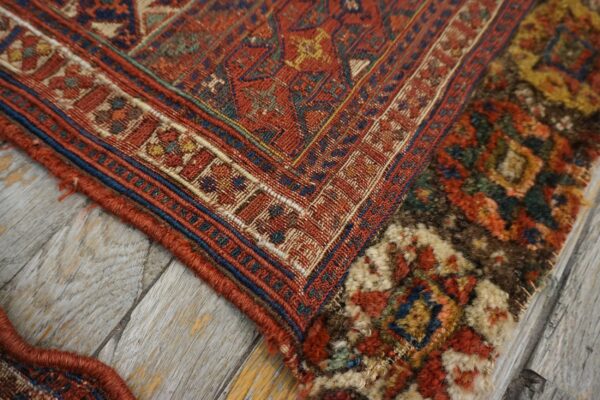 Rust-colored geometric rug detail showing flatweave and shaggy textures, resting on distressed gray wood planks.