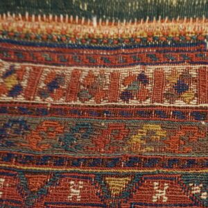 Detailed view of a flat-woven rug border showing intricate geometric patterns in red, blue, teal, and gold.