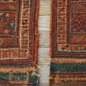 Two flat-woven rug pieces featuring red, blue, and gold geometric patterns rest on whitewashed wood.