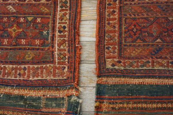 Two flat-woven rug pieces featuring red, blue, and gold geometric patterns rest on whitewashed wood.