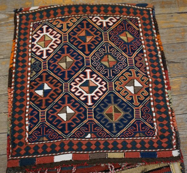 A small geometric rug in navy, rust, and white with sharp designs sits on distressed wood floorboards.