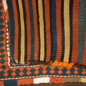 A flatweave rug with multicolored stripes and a diamond border rests on distressed wood flooring.