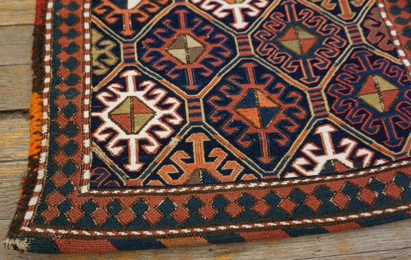 Navy and orange geometric rug with stylized motifs and patterned borders resting on wood floorboards.