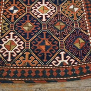 Geometric rug in navy, terracotta, and cream featuring intricate diamond patterns resting on wood planks.