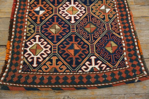 Geometric rug in navy, terracotta, and cream featuring intricate diamond patterns resting on wood planks.