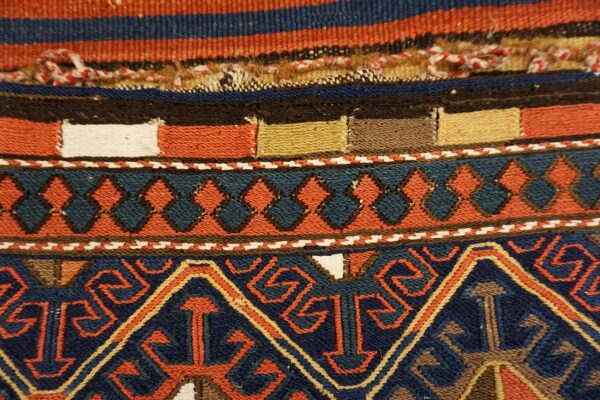 Detailed flatweave rug with navy, rust, and teal geometric diamonds and multicolored striped borders.