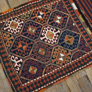 Geometric textile rug in navy, rust, orange, and white, with repeating medallions on distressed wood flooring.