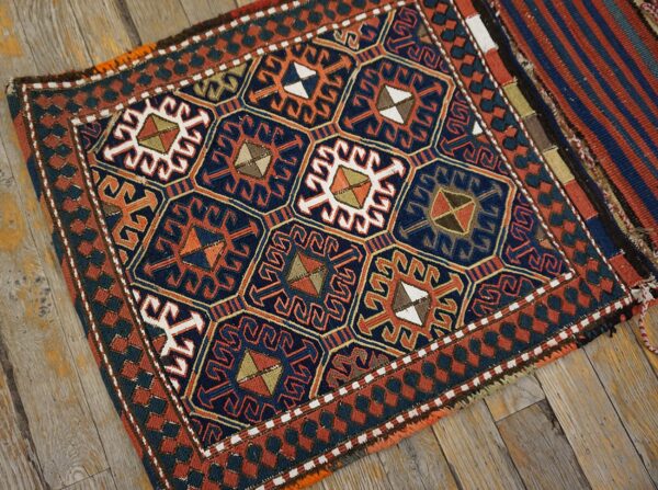 Geometric textile rug in navy, rust, orange, and white, with repeating medallions on distressed wood flooring.