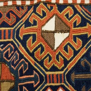 Geometric flatweave rug detail in navy, rust, and gold, featuring a central diamond motif.