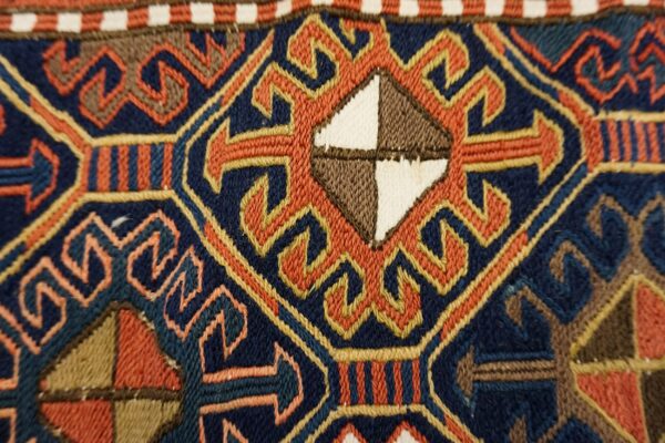 Geometric flatweave rug detail in navy, rust, and gold, featuring a central diamond motif.