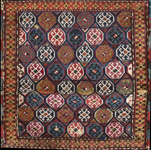 Low pile geometric rug with repeating octagonal motifs in red, blue, green, and cream, surrounded by a complex border.