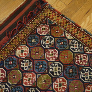 Multicolored rug with repeating octagonal and geometric borders rests on diagonal light brown hardwood flooring.