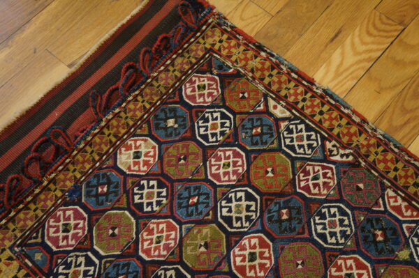 Multicolored rug with repeating octagonal and geometric borders rests on diagonal light brown hardwood flooring.