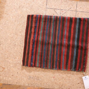 Small flatweave rug featuring vertical stripes of red, black, blue, and green on a wood work surface.