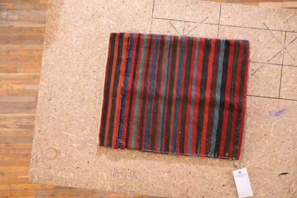 Small flatweave rug featuring vertical stripes of red, black, blue, and green on a wood work surface.