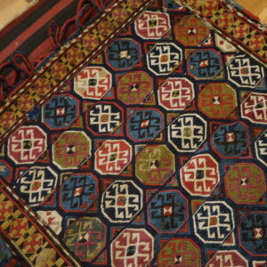 Colorful rug featuring repeating geometric octagonal motifs in navy, red, blue, and olive green on a wooden floor.