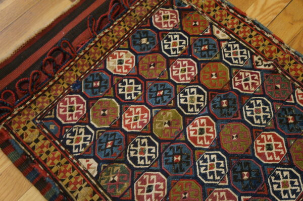 Colorful rug featuring repeating geometric octagonal motifs in navy, red, blue, and olive green on a wooden floor.