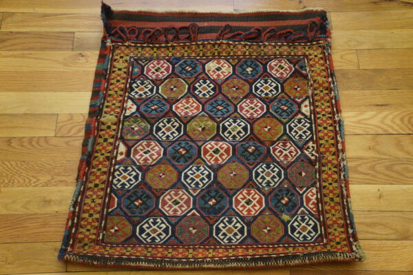Small rug with a repeating lattice of colorful red, blue, and green geometric medallions on hardwood flooring.