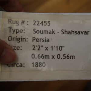 A hand holds a white label listing the rug number, type, origin, size, and 1880 date.