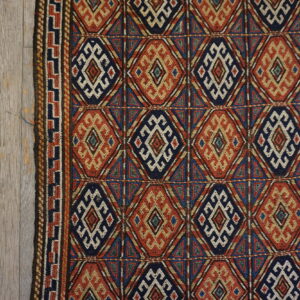 Geometric navy, rust, and cream diamond patterned rug on distressed wooden floorboards.