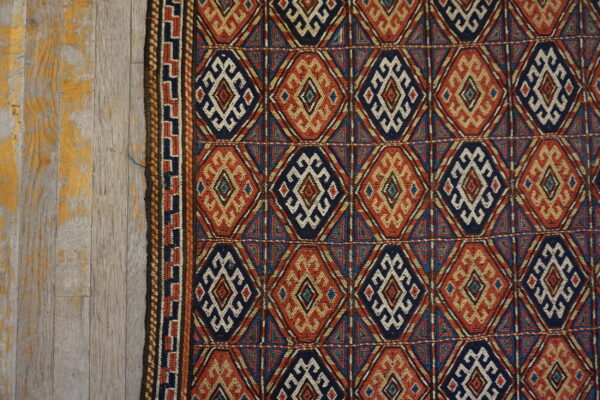 Geometric navy, rust, and cream diamond patterned rug on distressed wooden floorboards.