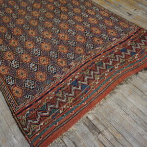 Rust, blue, and gold geometric rug with a detailed zigzag border lying on distressed gray wood plank flooring.