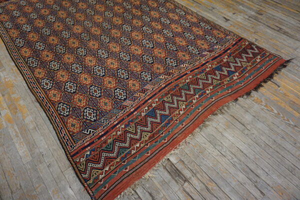 Rust, blue, and gold geometric rug with a detailed zigzag border lying on distressed gray wood plank flooring.
