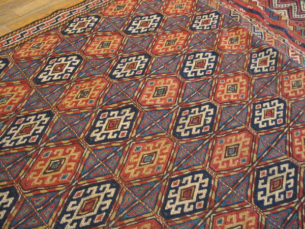 Intricate geometric diamond rug pattern in red, navy blue, and gold resting on wooden flooring.
