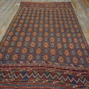 Rug featuring dense geometric diamonds and zigzag borders in red, navy, and gold on distressed wood planks.