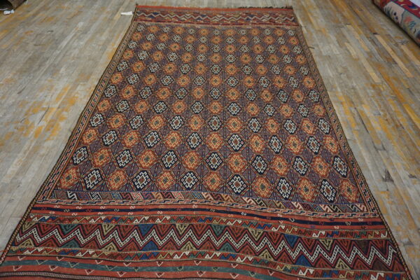 Rug featuring dense geometric diamonds and zigzag borders in red, navy, and gold on distressed wood planks.