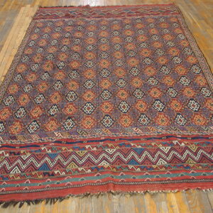 Geometric rug featuring repeating red, gold, and blue diamonds with wide patterned borders on a wood floor.
