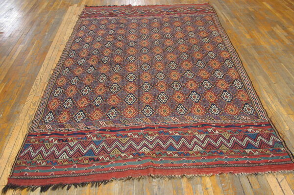 Geometric rug featuring repeating red, gold, and blue diamonds with wide patterned borders on a wood floor.