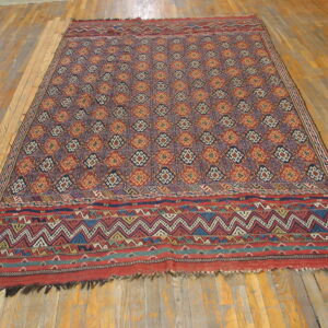 Red, navy, and orange geometric flatweave rug with wide, zigzag chevron borders on a wood floor.
