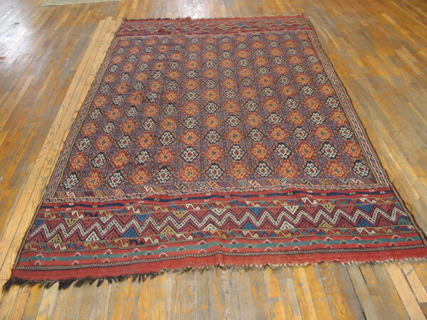 Red, navy, and orange geometric flatweave rug with wide, zigzag chevron borders on a wood floor.