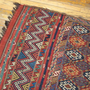 Red and blue flatwoven rug featuring zigzag borders and repeating geometric diamonds on light wood floors.