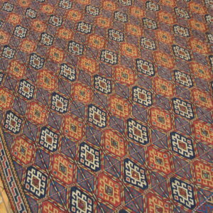 Flat-woven geometric rug with repeating navy blue and rusty red diamond medallions on a wood floor.