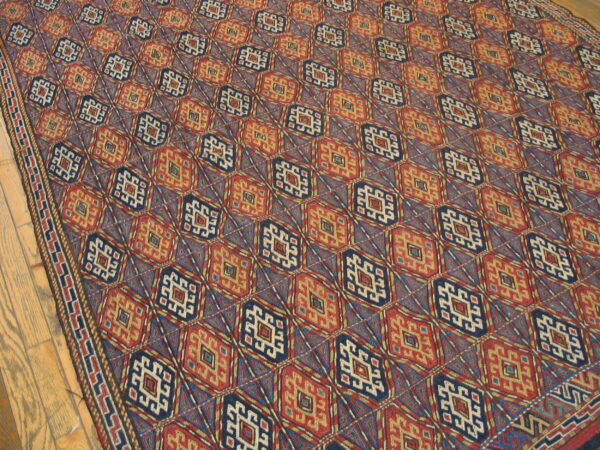 Flat-woven geometric rug with repeating navy blue and rusty red diamond medallions on a wood floor.
