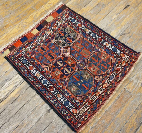 Rust and navy low-pile square rug featuring detailed geometric patterns lies diagonally on worn wood planks.