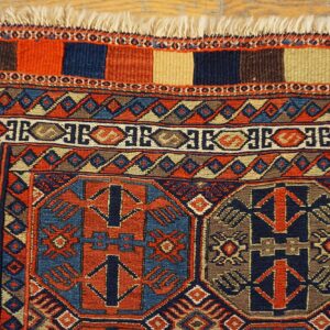 Geometric navy and rust rug detailing intricate patterns and fringe rests upon a light wood floor.