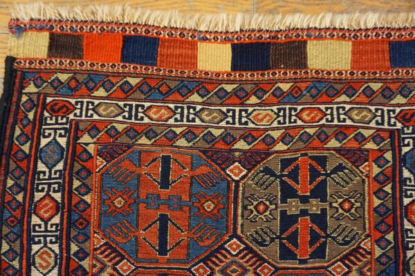 Geometric navy and rust rug detailing intricate patterns and fringe rests upon a light wood floor.