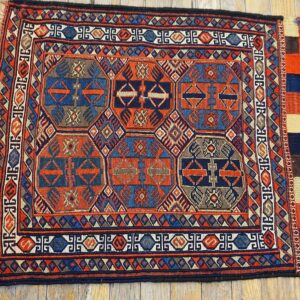 Detailed geometric tribal rug in rust and blue with multiple borders displayed on light hardwood planks.