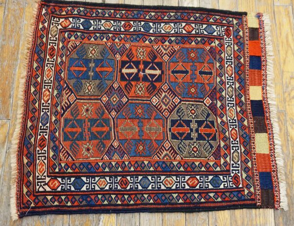 Detailed geometric tribal rug in rust and blue with multiple borders displayed on light hardwood planks.