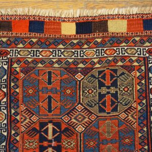 Complex geometric motifs in terracotta, navy, and tan cover this low-pile rug on rustic wood flooring.