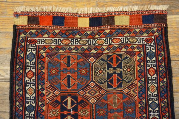 Complex geometric motifs in terracotta, navy, and tan cover this low-pile rug on rustic wood flooring.