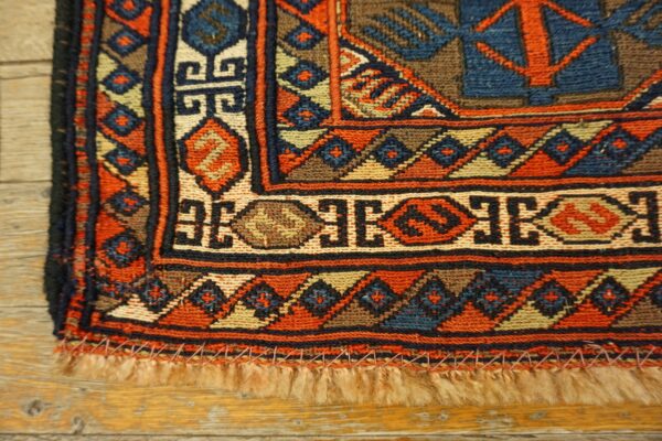 Flatwoven rug corner with dense geometric patterns in orange, blue, and beige, lying on wood planks.