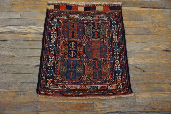 Intricately patterned red and blue small rug featuring geometric medallions rests on rustic wooden floor.