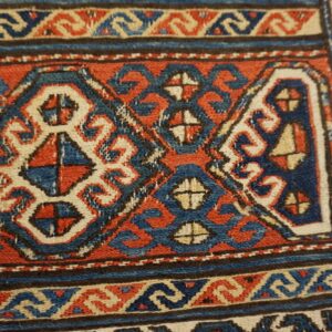 Geometric red, blue, and cream tribal patterns fill the low-pile texture of this detailed rug close-up.