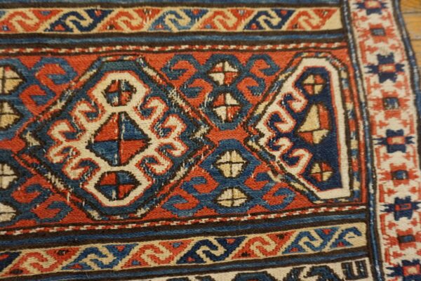 Geometric red, blue, and cream tribal patterns fill the low-pile texture of this detailed rug close-up.