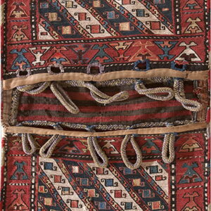 Long red and blue low-pile textile with diagonal motifs, bordered by stylized figures and central braided loops.