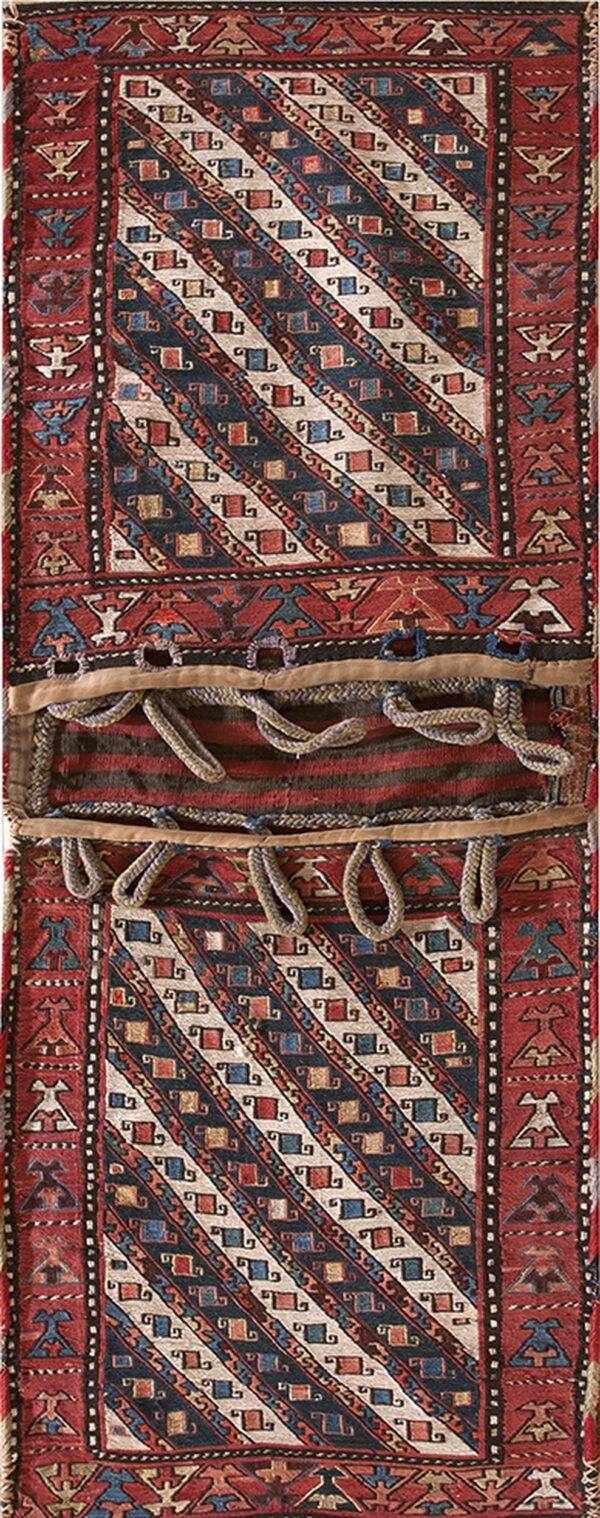 Long red and blue low-pile textile with diagonal motifs, bordered by stylized figures and central braided loops.